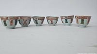 Photo showing six Chinese porcelain teacups with red and green decorative patterns on a white base, arranged in a row to highlight design and size.