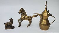 Three brass items on a white background: horse figurine with a raised front leg, sheep figurine on a flat base, and a teapot with handle and spout.