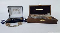 Wide angle image showing the tie pin, both pairs of cufflinks, and the gold plated razor in its wooden box, for identification and condition check.