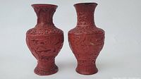 Front view of two red carved lacquer vases showing detailed bird and floral motifs to the body and neck