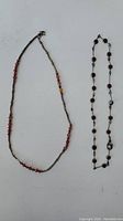Two necklaces laid flat on a white surface, both necklaces visible in full alongside a ruler to show size.