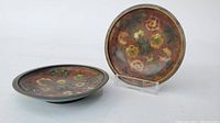Two small round cloisonne plates, floral pattern, one displayed upright and one flat.