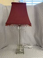 Full view of the 25-inch tall lamp with clear glass body and red fabric shade with beaded fringe.