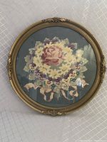 Front view of framed round needlepoint embroidery featuring floral bouquet design in gold-toned wooden frame.
