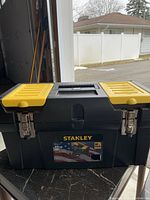 Closed view of the large Stanley tool box showing the black body, yellow compartment covers, metal latches, and handle.