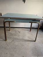 Side angle view of mid-century modern Arborite table showing chrome metal legs and underside of tabletop with extension leafs.