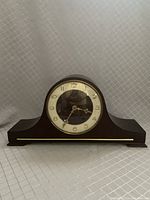 Front view of Auchincloss German mantle clock with round face, Arabic numerals, dark wood case, and glass cover