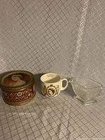 Photo of candy tin, mug, and glass creamer displayed on fabric background showing size and design.
