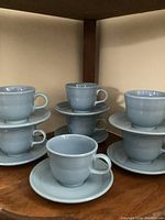 Seven Fiesta Ware cups stacked with matching saucers on wooden shelving, showing full set.