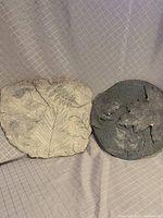 Two garden stepping stones or wall plaques shown side by side, highlighting their shape and relief design.