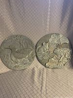 Photo showing two round garden plaques with raised wildlife designs: duck and frogs motifs.