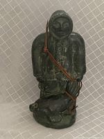 Front view of the hand carved sculpture showing the seal hunter in traditional clothing with a spear and a dog.