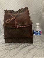 Full view of the carved wood and woven fish carrying basket next to a water bottle for size reference.