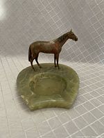 Angled front view showing the horse figurine mounted on a green marble ashtray with three notches.
