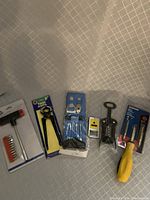 Photo of six miscellaneous tools laid out on fabric surface including T-screwdriver with bits, wire stripper, corkscrew, yellow screwdriver, bottle opener, and utility knife.