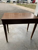 Side view of the wooden piano bench showing the finished top and turned legs with metal caps.