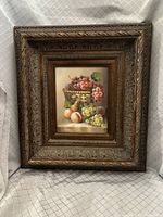 Frontal view of the framed still life painting depicting fruit on a table with a carved ornamental dark wood frame.