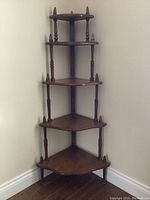 Full view of the wooden corner what not shelf with its five graduated triangular shelves and turned wooden supports.