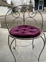 Front view of white wrought iron vanity chair with purple round tufted seat cushion, showing scrollwork on backrest