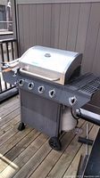 Full view of Nexgrill propane gas grill on wooden deck showing overall structure, control knobs, side shelves, wheels, and propane tank.