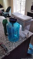 Brita UltraMax water dispenser with adjacent blue travel jug and green travel bottle. Shown on countertop with clear spigot.
