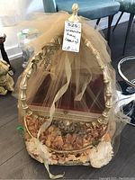 Photo shows metal rectangular serving tray with bamboo-style handle arching over the top, decorated with peach and white artificial flowers around the base and covered with beige tulle fabric.