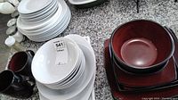 Multiple stacks of solid white dishes including bowls, dinner plates, and side plates along with two dark-colored mugs.