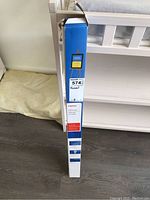 Photo showing tall, narrow blue box with Staples branding and label for an oak easel.