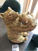 Resin figurine showing a gold-tone bear holding a cub with detailed textured fur, seated pose.