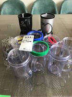 Photo of two Magic Bullet blender bases (one black, one silver/black) and multiple clear blending cups with colored sealing rings and lids on a table.