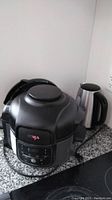 Photo showing the black Ninja cooker placed on a granite countertop, showing its exterior and handle.