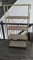 Front view of shelving unit showing four woodgrain shelves and gold tone steel frame with some scuffs visible.