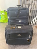 Two black softside suitcases stacked, larger on bottom smaller on top, showing front with zippers and handles