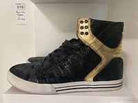 Side angle of one black and gold Supra Skytop sneaker showing overall style, colors and worn condition.
