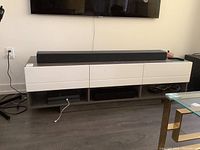 Full front view of the TV stand showing white drawers, dark wood top and cubbies below with items inside.