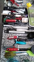 Photo showing assorted kitchen utensils including knives, grater, silicone spatulas, peeler, juicer, and tongs in black tray