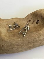Pair of 10K white gold wishbone earrings with clear stones displayed on a wooden surface, side angle showing front and back.