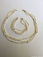 Photo of the laid flat triple strand freshwater pearl necklace and matching bracelet showing the overall design, pearls, and gold beads.