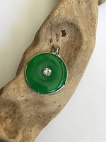 Front side of the pendant showing the smooth green disc stone with central clear rhinestone and metal frame with bail.