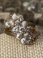 Close-up image showing gold-tone ring with cluster of 15 clear stones arranged in a decorative pattern at the top, prong set, on a split shank band. Marked 14KGE.