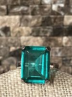 Close-up of the large green emerald-cut stone set in sterling silver band with four prongs, showing its vibrant color and clarity.