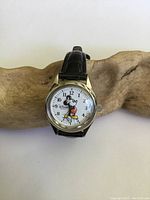 Front view of vintage Disney Mickey Mouse wristwatch with white dial, colorful Mickey graphic, and black genuine leather strap.