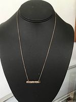 Sterling silver necklace displayed on a black bust showing thin chain and scroll pendant
