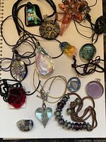 Top-down photo of a variety of artisan handmade glass and stone jewelry including pendants and necklaces lying flat on a notebook.