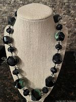 Full view of the necklace displayed on a stand, showing the alternating green/black faceted stones and smaller black beads.