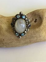 Front view of sterling silver ring with large oval moonstone surrounded by smaller round blue and purple gemstones set in a beaded design.