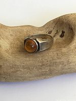 Front angled view of the sterling silver ring with round Baltic amber set on a wooden display.