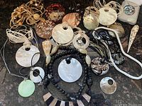 Photo showing a variety of shell and mother of pearl necklaces laid out on a dark surface, illustrating the assortment of designs and types.