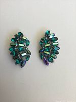 Pair of vintage clip-on earrings with bright blue, purple, and green rhinestones, laid flat on white background