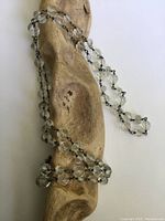 Full view of the clear faceted crystal bead necklace draped over a wooden form, showing length and bead clarity.